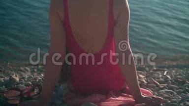 一个穿着红色一件泳衣的漂亮女孩坐在夕阳下的海滨。 那个女孩坐在相框里。